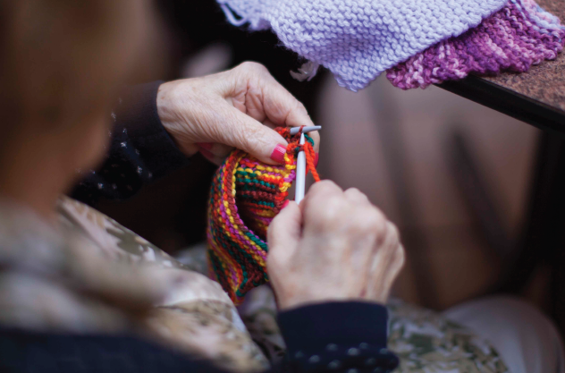 Persona mayor tejiendo con agujas una bufanda multicolor en Cohabitam